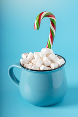 Mug of hot chocolate with marshmallows on top and stick a Lollipop on a blue background. Cozy winter card