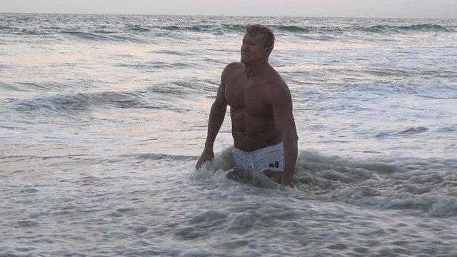 Muscular male bodybuilder in the surf at the beach 
