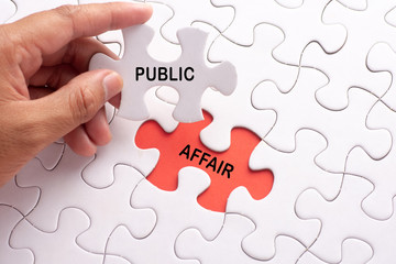 Hand holding piece of jigsaw puzzle with word PUBLIC AFFAIR