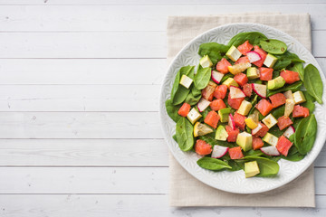 Poke Hawaiian salad with salmon, avocado spinach and vegetables in a plate on a white table.