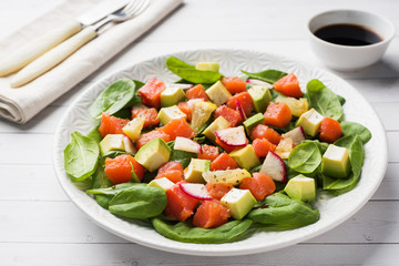 Poke Hawaiian salad with salmon, avocado spinach and vegetables in a plate on a white table.
