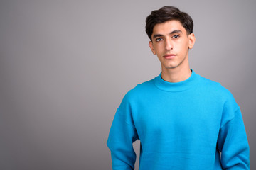 Young handsome Persian teenage boy against gray background