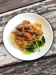 yellow noodles with decicious cooked duck in white plate on old wood table