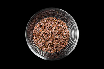 Flax seeds in a glass cup on a black background, top view