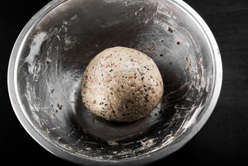 Preparation of healthy rye loaves: ready-made dough in a metal bowl on a black background, top view