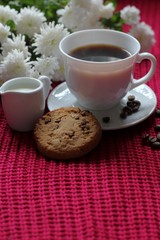 Traditional continental breakfast, cup of coffee espresso with milk, pile of delicious chip cookies tied with twine and white flowers on a red knitted background. Good morning concept. Enjoy slow life