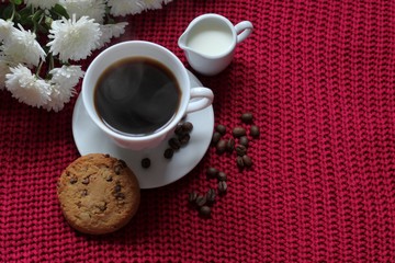 Traditional continental breakfast, cup of coffee espresso with milk, pile of delicious chip cookies tied with twine and white flowers on a red knitted background. Good morning concept. Enjoy slow life