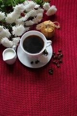 Traditional continental breakfast, cup of coffee espresso with milk, pile of delicious chip cookies tied with twine and white flowers on a red knitted background. Good morning concept. Enjoy slow life