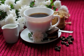 Obraz na płótnie Canvas Traditional continental breakfast, cup of coffee espresso with milk, pile of delicious chip cookies tied with twine and white flowers on a red knitted background. Good morning concept. Enjoy slow life