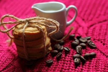 Coffee beans with milk, pile of delicious chip cookies tied with twine on a red knitted background with a pattern. Good morning concept. Enjoy slow life