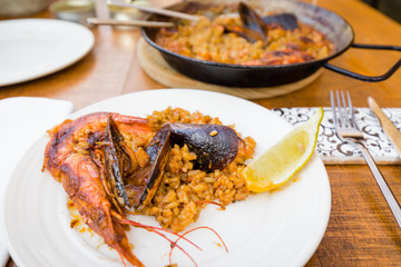 Seafood Paella in a traditional pan and served on white plate against wooden background