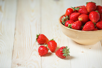 Fresh strawberries in a bowl on wooden table with low key scene.