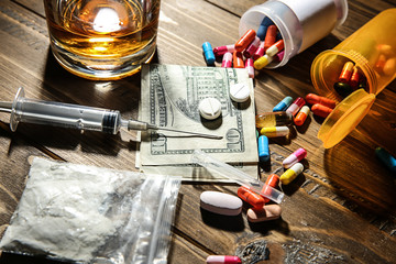 Drugs, money and alcohol on wooden background. Concept of addiction