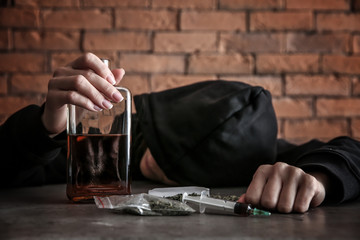 Female junkie with alcohol and drugs at grey table. Concept of addiction