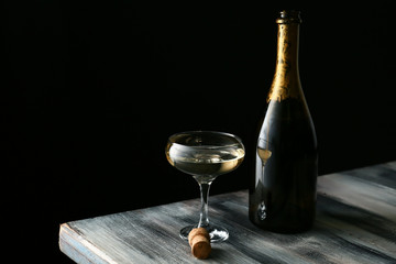 Glass and bottle of champagne on wooden table against dark background - Powered by Adobe