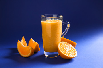 Glass cup of tasty yellow smoothie and cut orange on color background