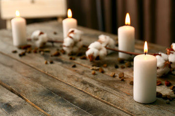 Burning candles with cotton flowers on wooden table