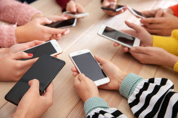 Young people using mobile phones at wooden table, closeup. Concept of addiction