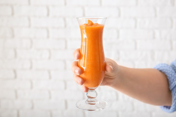 Woman holding glass of tasty orange smoothie on light background