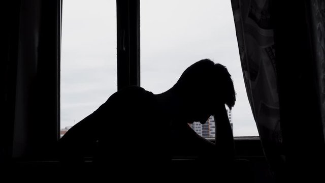 Silhouette of desperate sad man in the dark in front of a window
