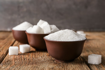 Bowls with refined sugar on wooden background
