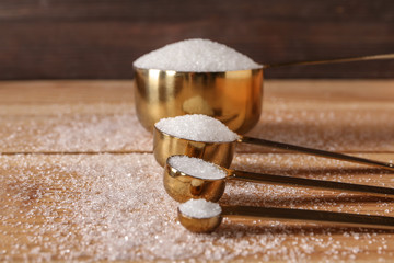 Spoons with refined sugar on wooden background