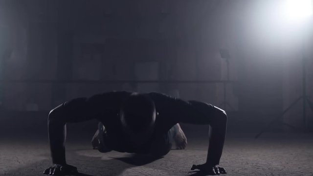 Professional athlete doing push-ups in dark smoky gym. Boxer training in elastic bandages. Sport concept. Silhouette on dark background