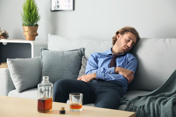 Drunk man sleeping on sofa near table with bottle and glass of whiskey. Alcoholism concept