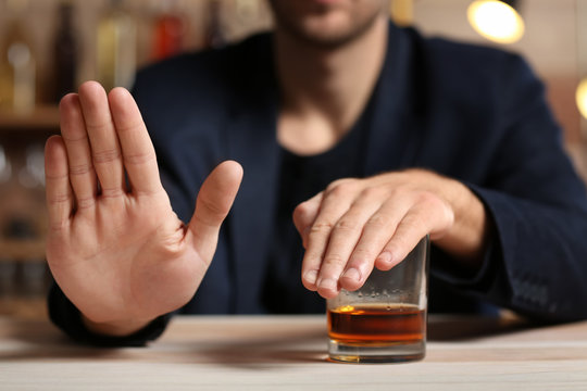 Man with glass of whiskey at table refusing to drink
