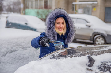 Clearing the snow girl from the car in the winter in the yard with a brush