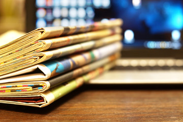 Newspapers and computer. Business magazines and blurred screen of laptop on background. Tabloid...