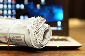Newspapers and computer. Business magazines and blurred screen of laptop on background. Tabloid journals and  notebook connected with internet - different sources of information and news