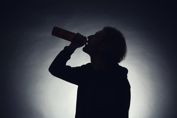 Silhouette of man drinking beer on dark background. Alcoholism concept