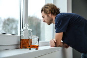 Bottle and glass of whiskey on windowsill in flat of depressed young man. Alcoholism concept