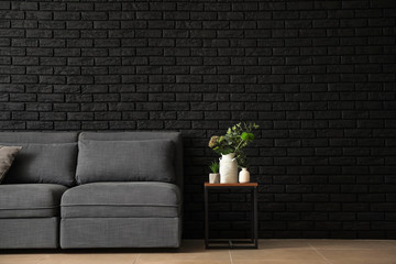 Stylish interior of room with comfortable big sofa near dark brick wall