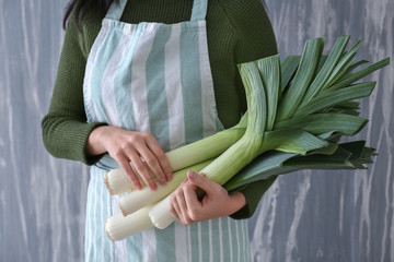 Woman holding raw leeks against grey background