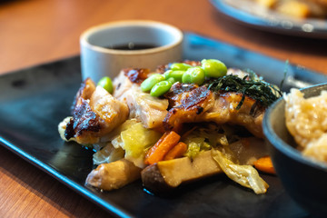 close up of chicken steaks with cup of sauce on the black plate. Green peas and Japanese seaweed on chicken steaks with white cabbage, carrots and mushrooms in the restaurant
