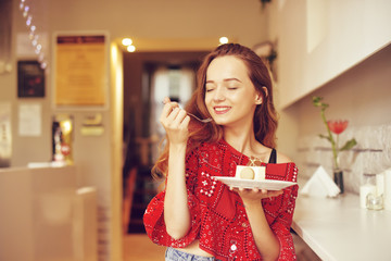 The girl in the bakery eats dessert. Beautiful model in a cafe eats sweets and smiling. Beautiful girl in a red sweater with long hair eats in a restaurant alone, diet.
