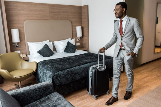 smiling african american businessman with travel bag in hotel room