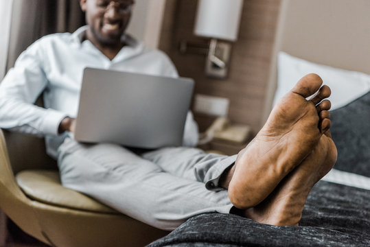 selective focus of barefoot african american man using laptop in hotel room