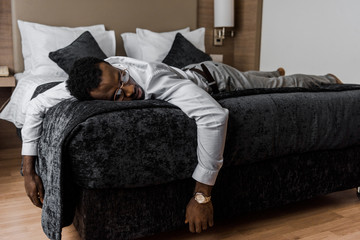 exhausted african american man sleeping on bed in hotel room