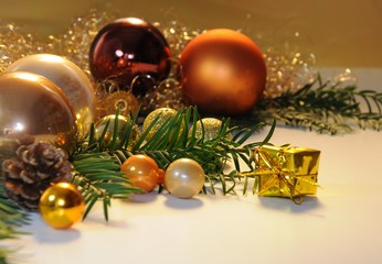 Fototapeta na wymiar Goldene Weihnachtskugeln, Tannenzweige, Tannenzapfen und Schnee auf einem Gabentisch vor goldenem Hintergrund