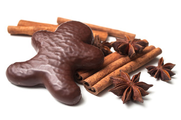 closeup of christmas gingerbread chocolate coated biscuit in shaped man with anise flower and cinnamon stick on white background