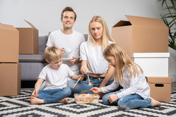 Picture of happy couple with children eating rice with shrimps sitting on floor