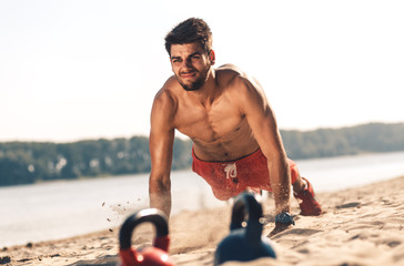 Young man doing fitness workout at a beach on a sunny day.