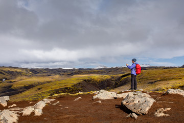 Obraz premium A young woman with a backpack travels around Iceland. Front view of a tourist walking through a mountainous area on a sunny day.