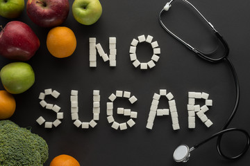 "no sugar" lettering made of cubes among fruits and vegetable on black
