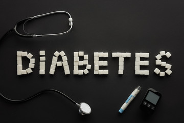 top view of "diabetes" lettering made of sugar cubes with medical equipment on black