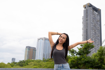 Fototapeta na wymiar Young beautiful Asian woman relaxing at the park with arms raised