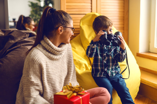 Mother and son at living room. Mother holding Christmas gift while son sitting in bean bag and holding binoculars wrong.